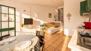 Ein kleines Hotelzimmer mit Essbereich, einem Bett, einem Fernseher und einer Küchenzeile.