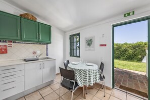 A kitchen with green cabinets, a dining table with a checkered tablecloth, and a view of a garden through a sliding glass door. - Bright apartment with access to a shared pool (Fuseta)