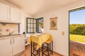 Eine kleine Küche mit Essbereich, ein Fenster mit Blick auf Grünflächen und eine dekorative Blattschmuckleiste.