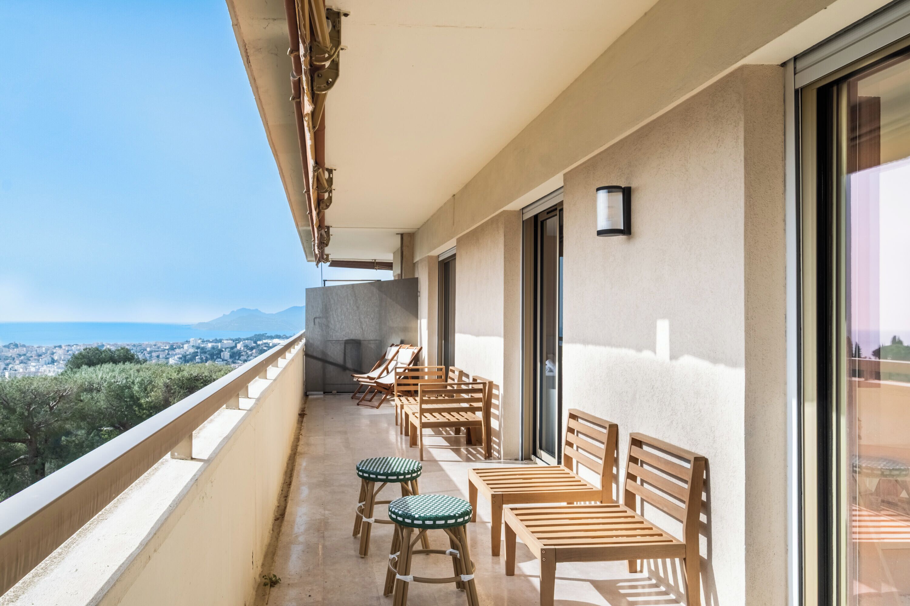 Ein Balkon mit Holzmöbeln, darunter Stühle und Tische, mit Blick auf eine Stadtlandschaft und Berge.