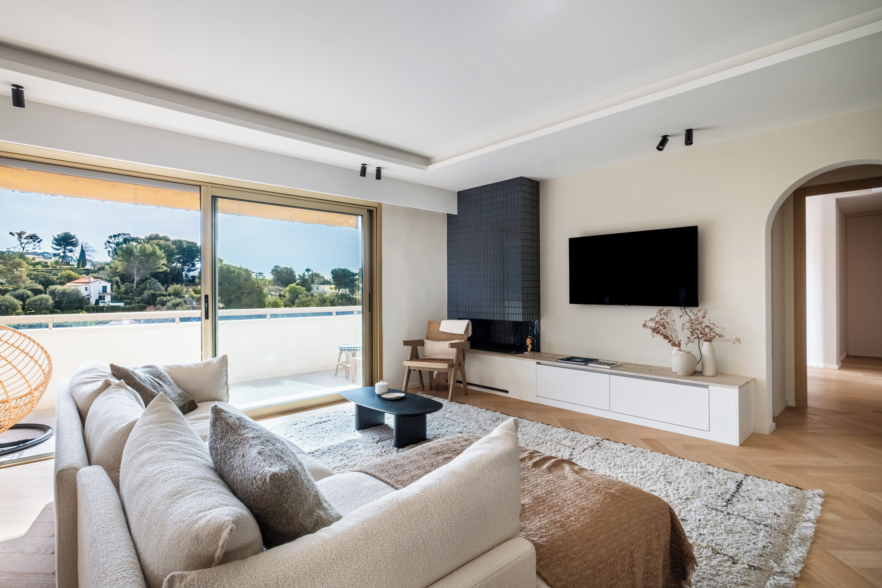 A modern living room with a large window, a sofa, a coffee table, and a flat-screen TV.