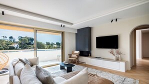 A modern living room with a large window, a sofa, a coffee table, and a flat-screen TV. - Terrasse vue Baie de Cannes - Welkeys (Le Cannet)