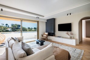 Ein modernes Wohnzimmer mit großem Fenster, einer Couch, einem Couchtisch und einem Flachbildfernseher.