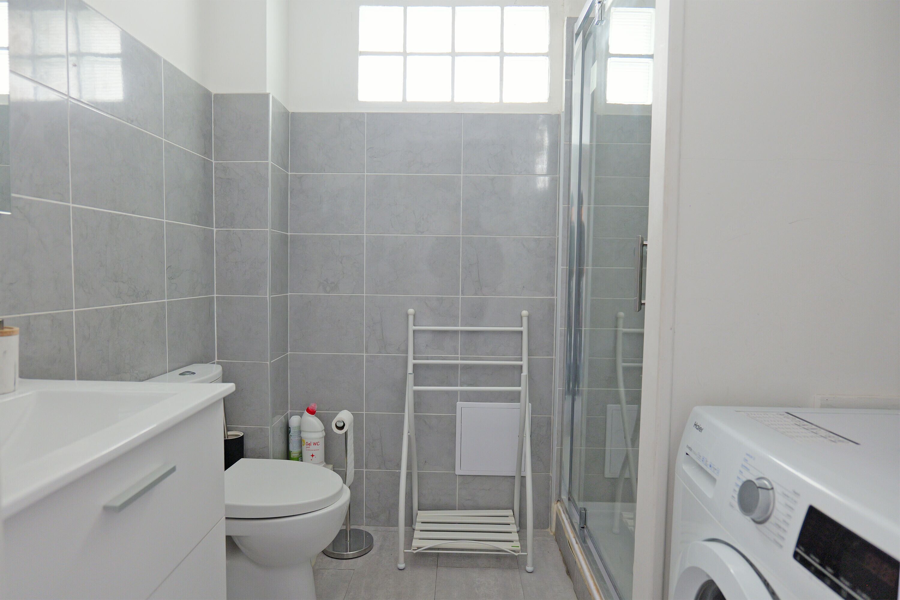 A modern bathroom with a toilet, a washing machine, and a glass shower enclosure.