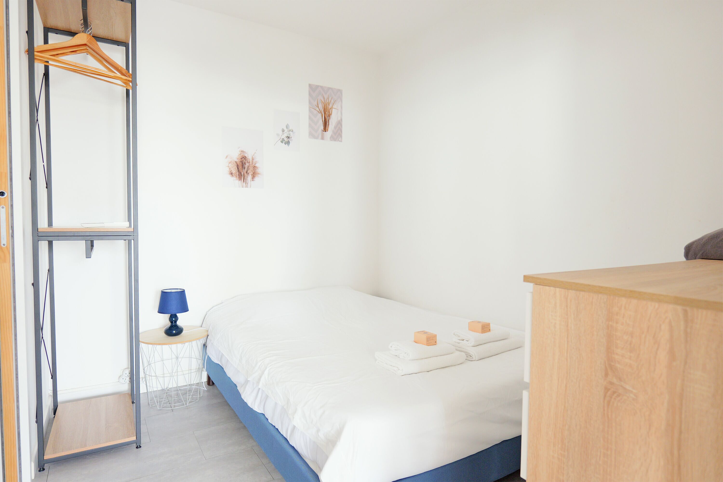 Ein Schlafzimmer mit einem Bett, einem Nachttisch mit Lampe, einem Holzschrank und einem Kleiderhaken.