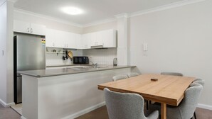 Una cocina moderna con armarios blancos, un refrigerador de acero inoxidable, un microondas y una mesa de comedor de madera con cuatro sillas.