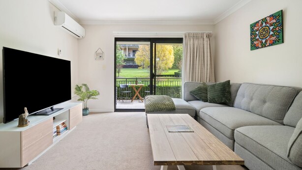 Sala de estar con televisor de pantalla plana, sofá, mesa de centro y balcón con vista a un jardín.