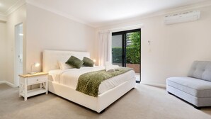 Un dormitorio con cama, mesita de noche, lámpara y un sofá gris.