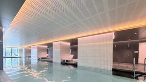 An indoor swimming pool with tiled walls and ceiling, lounge chairs, and a clear view of the outside. - Modern 1-bedroom apartment with gym and pool access, centrally located near cafes, restaurants, and public transport—perfect for a comfortable city stay. (Southbank)