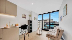 A modern kitchen with a bar area, a sofa, and a large window with a city view. - Modern 1-bedroom apartment with gym and pool access, centrally located near cafes, restaurants, and public transport—perfect for a comfortable city stay. (Southbank)