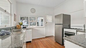 A modern kitchen with white cabinets, a stainless steel refrigerator, a gas stove, and a window with a view of snow-covered trees. - Misty Pines in Leura (Leura)