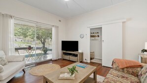 A living room with a sofa, a coffee table with a plant, a television on a wooden stand, and a dining area with a table and chairs. - Misty Pines in Leura (Leura)