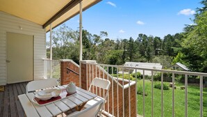A balcony with a table set for two, a brick wall, and a view of a green garden and neighboring houses. - Misty Pines in Leura (Leura)