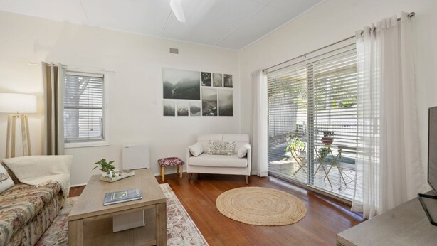A living room with a sofa, armchair, coffee table, and a view through large windows. - Misty Pines in Leura (Leura)