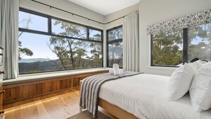 A bedroom with a large window, wooden flooring, and a bed with white bedding. - Sunset Retreat in Mount Victoria (Mount Victoria)