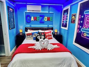 Ett sovrum med en säng, kuddar och en neonreklamskylt med texten ”GAMEZONE”.