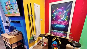 Una stanza colorata con un espositore per Nintendo Switch, una scopa e un neon pubblicitario di giochi retrò.