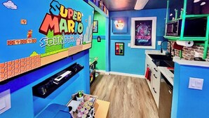 Una stanza con un muro a tema Super Mario, un neon e uno scaffale con diversi oggetti.