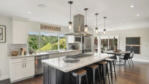 Une cuisine moderne dotée d’un grand îlot central, de tabourets de bar et offrant une vue sur l’extérieur.