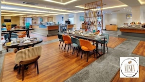 A modern cafe with wooden flooring, orange and grey chairs, and a central serving area with a wooden rack. - Amanora the Fern Hotels And Club (Pune)