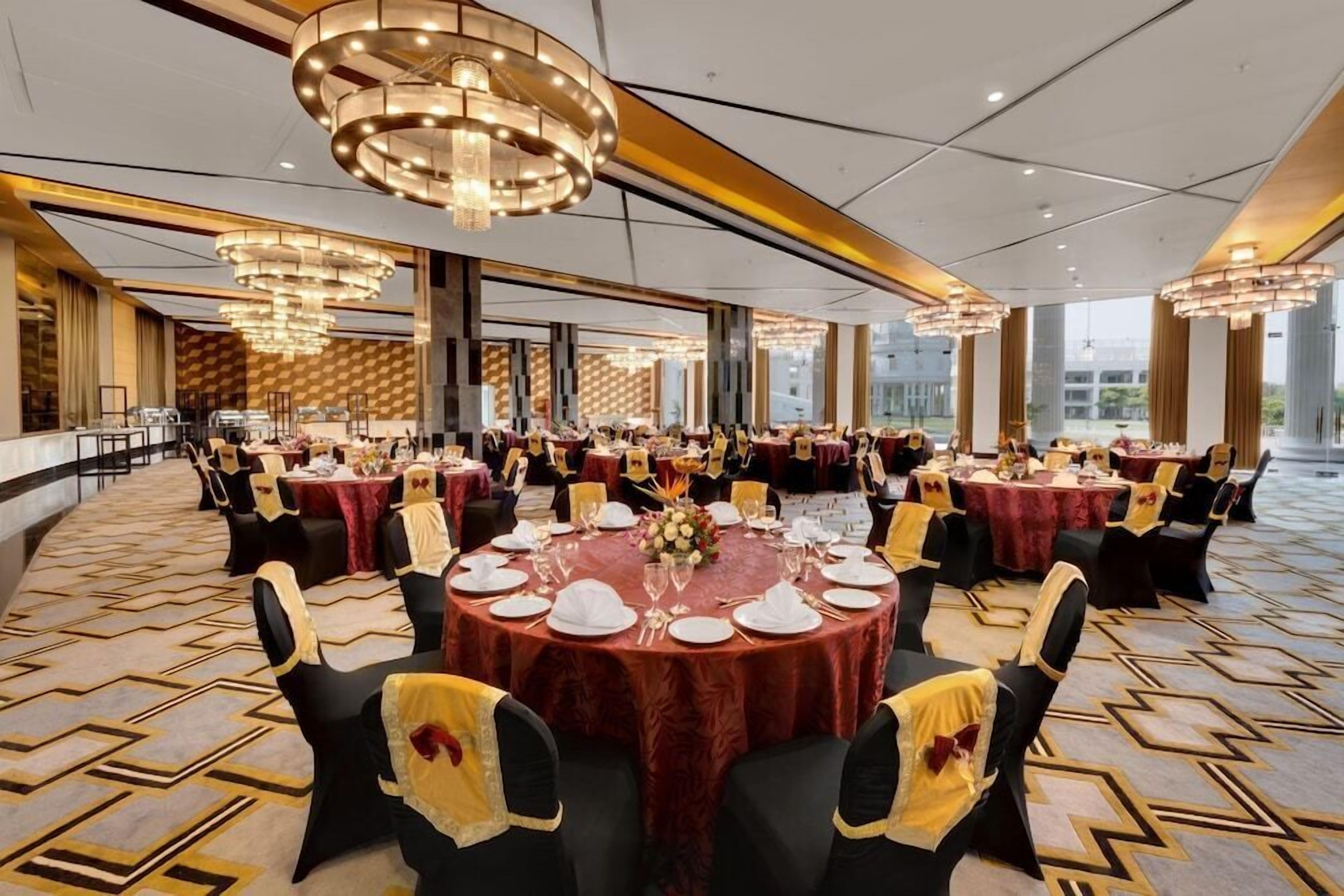 A large banquet hall with round tables set for dining, featuring chandeliers and a patterned carpet.