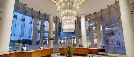 A spacious lobby with a large chandelier, reception desks, and a patterned floor.