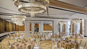 A banquet hall with round tables and white chairs, large chandeliers, and a patterned carpet. - Amanora the Fern Hotels And Club (Pune)
