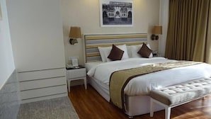 A hotel room with a large bed, a bedside table, a nightstand, a bench, and a wall-mounted lamp. - Amanora the Fern Hotels And Club (Pune)