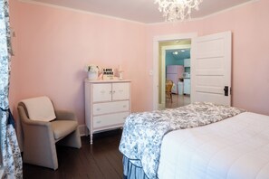 Une chambre à coucher comprenant un lit, une chaise, une commode et une porte donnant sur une autre pièce.