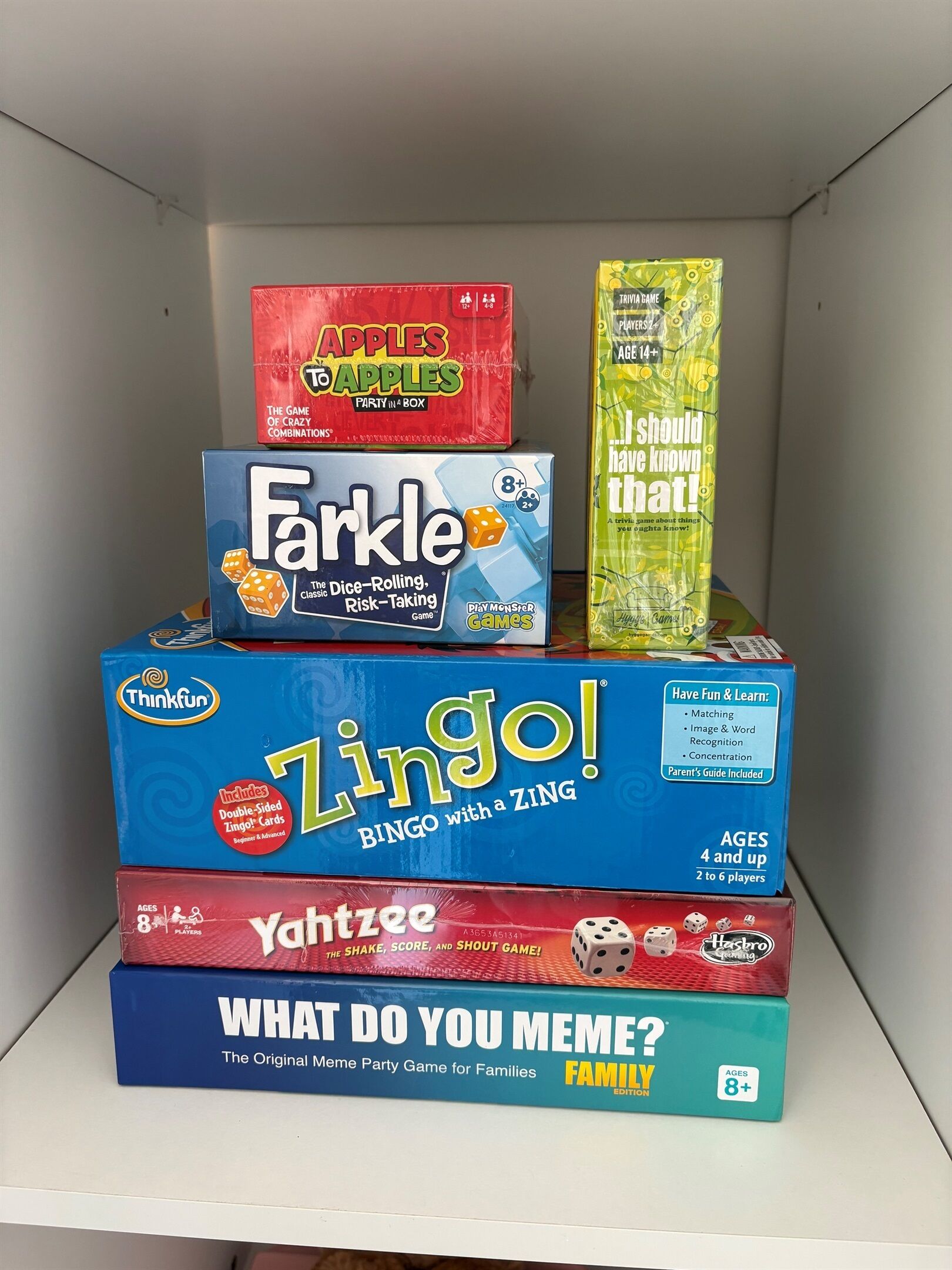 A shelf with various board games including Apples to Apples, Farkle, Zingo!, and What Do You Meme?