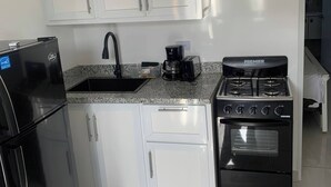 A kitchen with white cabinets, a black refrigerator, a coffee maker, and a stove. - Condo Neuf à Sosua Près de Tout et Équipé, 207 (Sosúa)