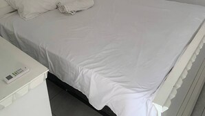 A white bed with pillows, a bedside table, and a wall-mounted air conditioner. - Condo Neuf à Sosua Près de Tout et Équipé, 207 (Sosúa)