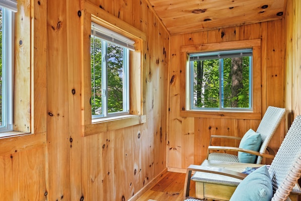A wooden cabin interior with two windows, a wooden chair, and a small table.