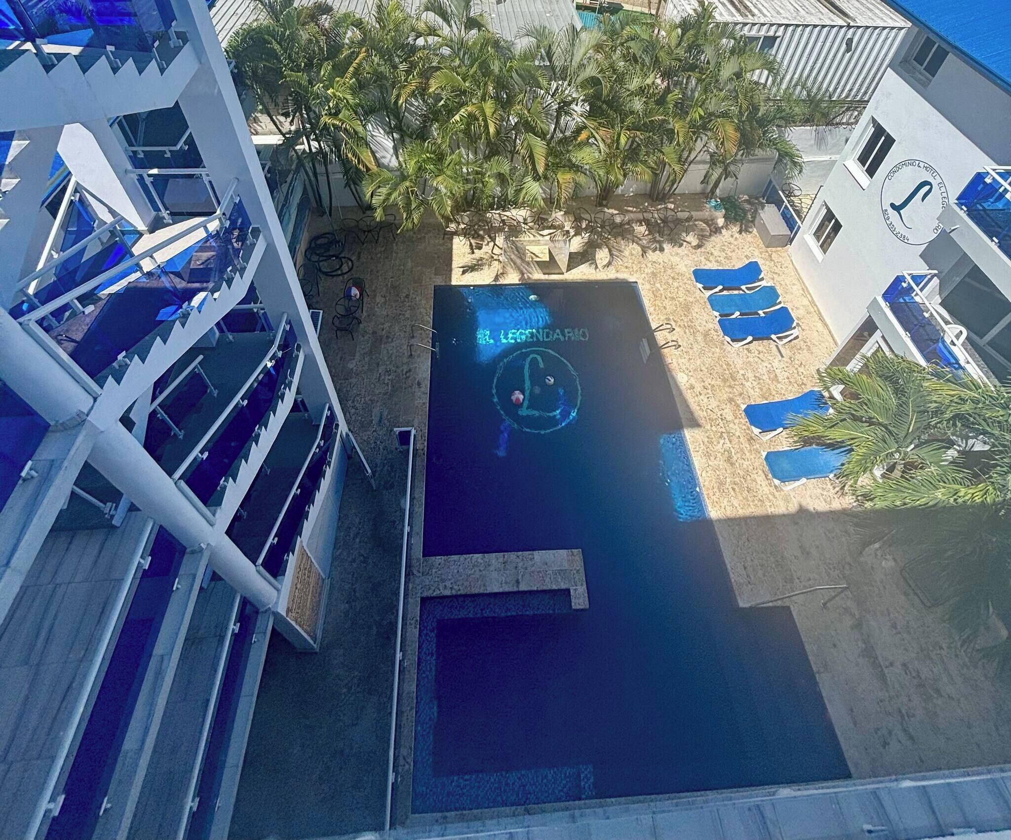 Une piscine sur le toit, ornée du logo « LEGENDARIO », entourée de chaises longues et de palmiers.