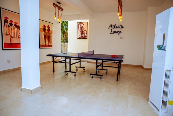 A spacious room with a ping pong table, artwork on the walls, and a refrigerator.