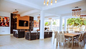 A spacious living area with a large wooden dining table, comfortable seating, and a flat-screen TV mounted on the wall. - Atlantic Shores Resort (Lagos)