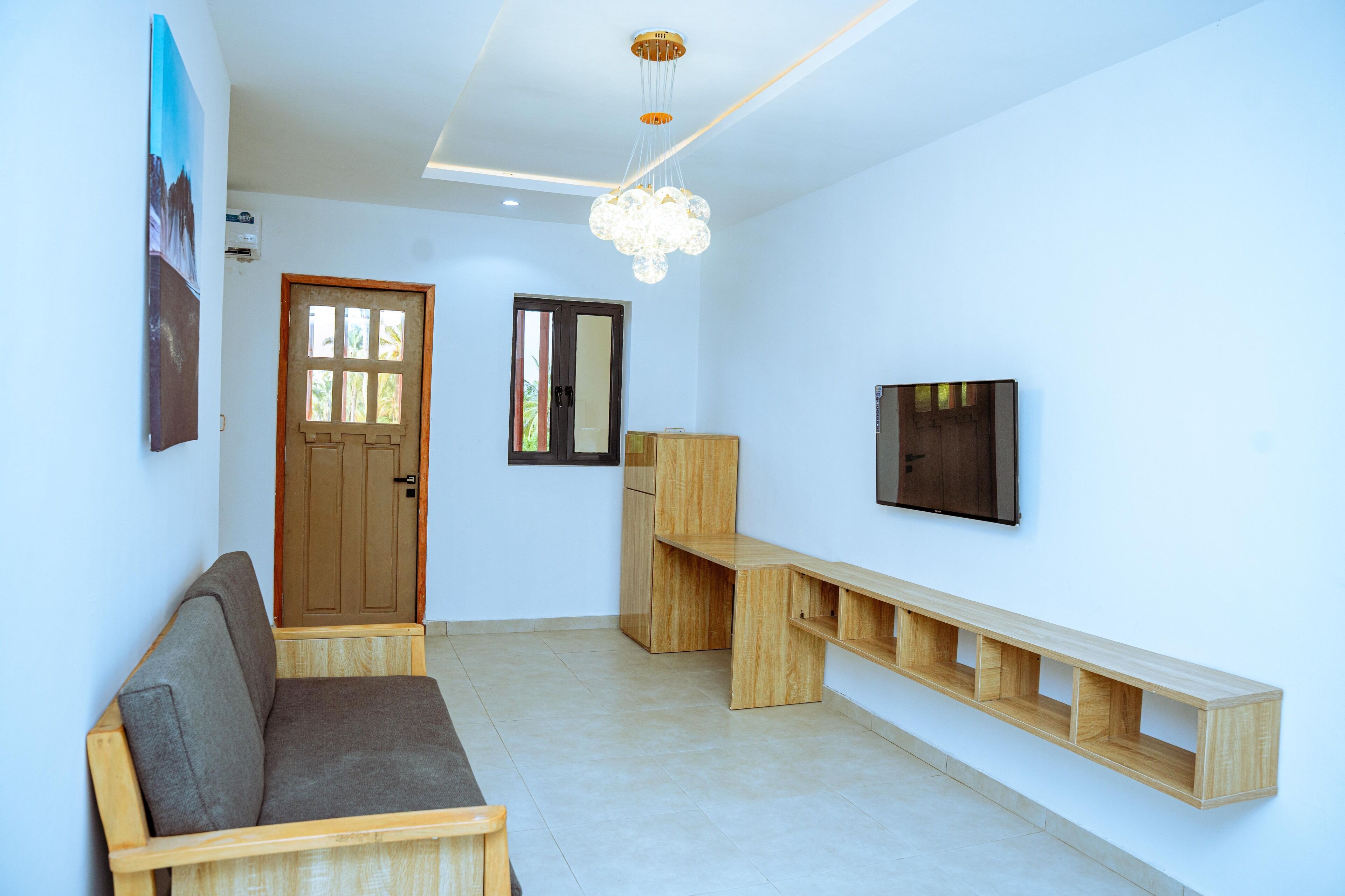 A modern living room with a wooden bench, a sofa, a TV mounted on the wall, and a ceiling light fixture.