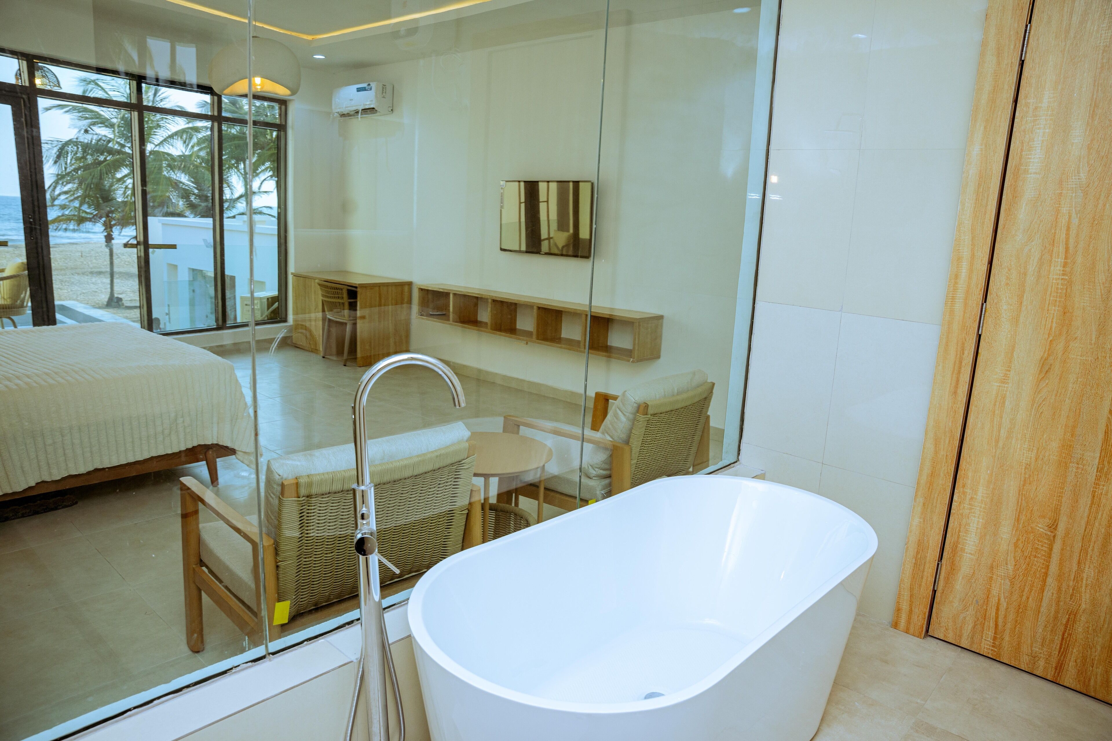 Une salle de bain moderne avec une baignoire sur pieds, des meubles en osier et une grande fenêtre donnant sur une plage.