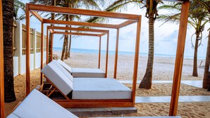 A wooden pergola structure with white cushioned lounge chairs on a sandy beach. - Atlantic Shores Resort (Lagos)