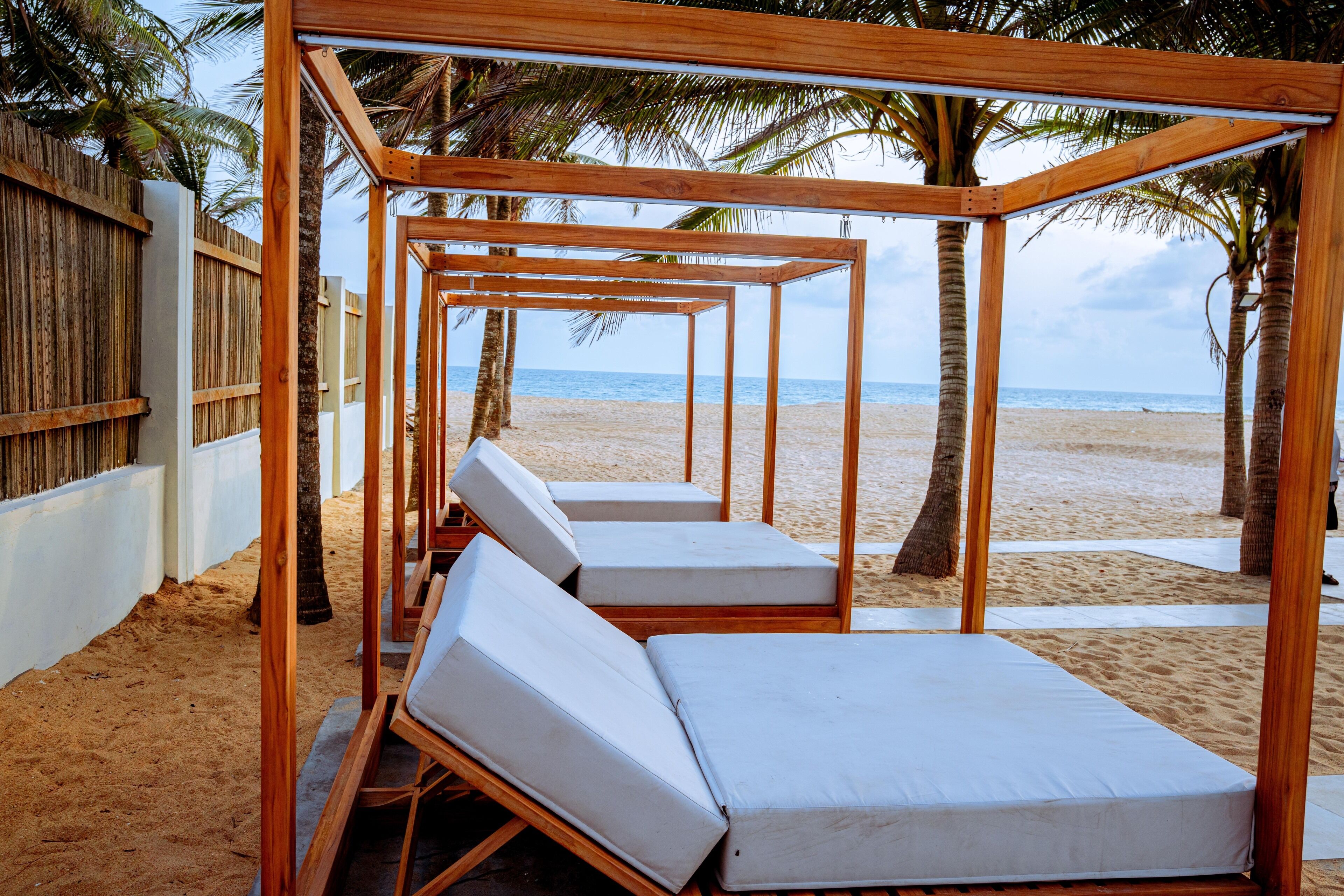 A beachside lounge area with wooden pergolas and white cushioned lounge chairs.