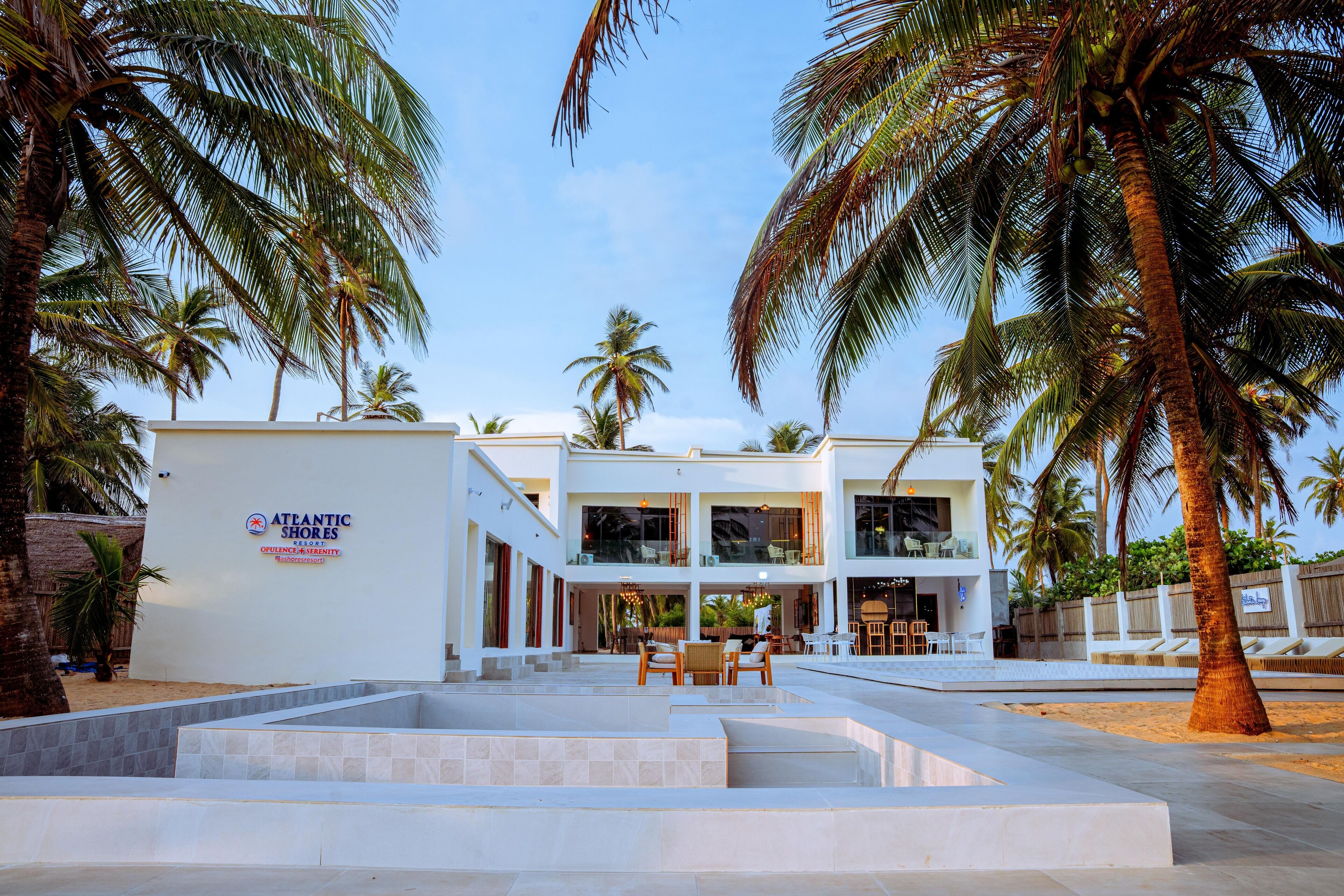 A modern hotel with a pool area, palm trees, and a sign reading "Atlantic Shores."