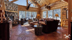 Ein Blockhaus-Interieur mit Steinfußboden, Kamin, Ledersofas und einer Kristallleuchtre.