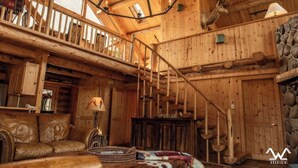 Ein Holzblockhaus-Interieur mit einer Holztreppe, einem Ledersofa, einem Kamin und einer Dekoration mit einem Hirschkopf.