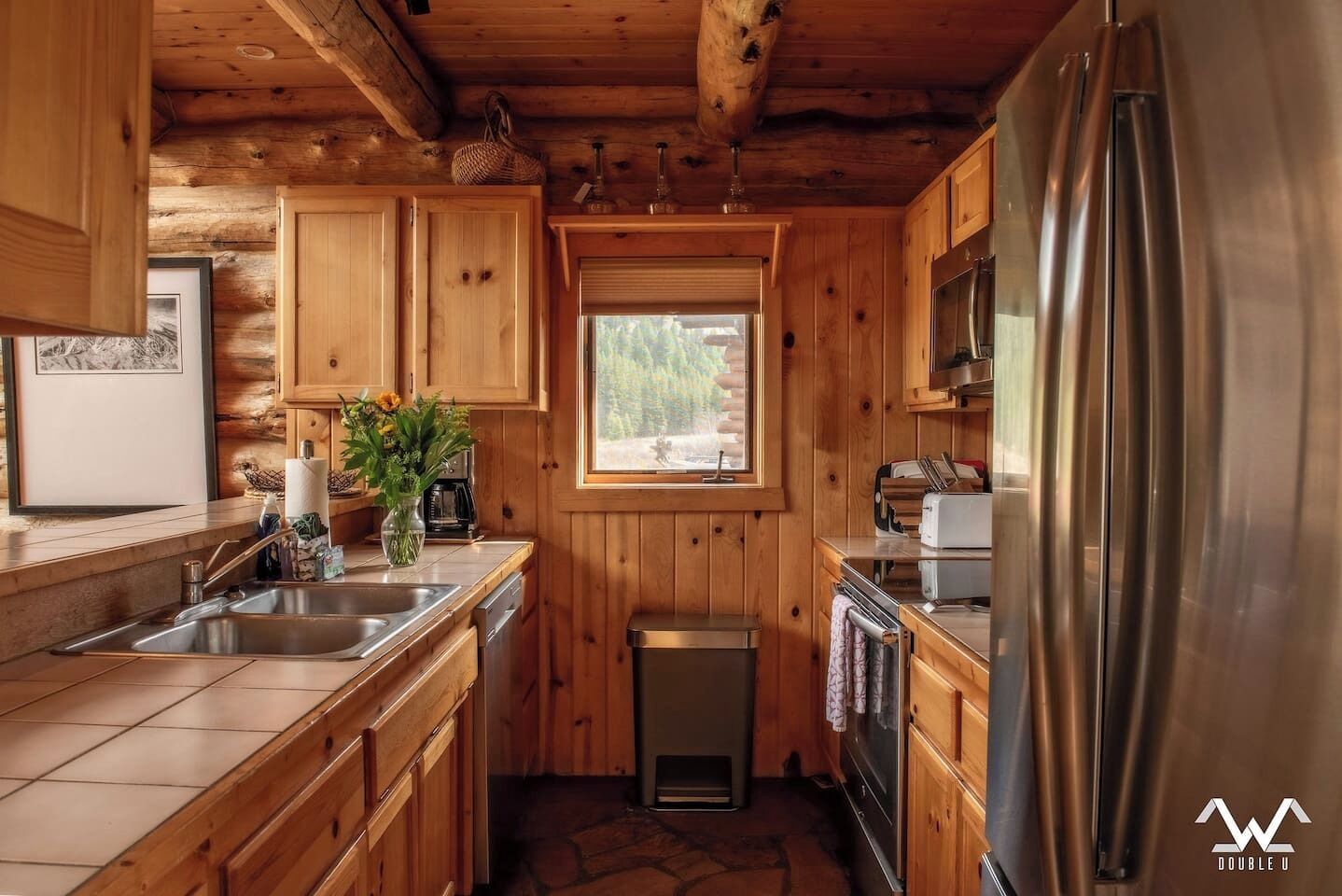 A compact kitchen with wooden cabinets, a stainless steel sink, a built-in oven, and a refrigerator.