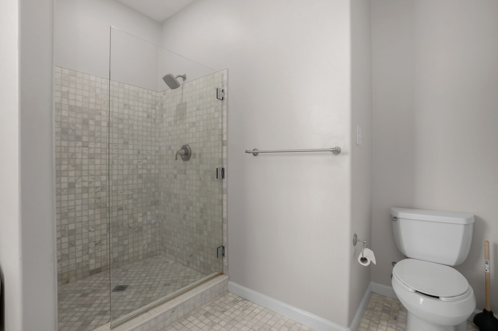 Une salle de bain avec une douche à parois de verre, des toilettes et une barre d’appui.