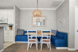 Un comedor con un sofá azul, sillas blancas, una mesa de madera y una lámpara colgante.
