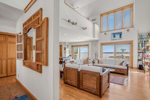 A spacious living room with a large white sofa, wooden furniture, and a view of the outdoors through large windows. - Sunrise View | Waterfront, Kayaks, Gorgeous Sunrises! (Chincoteague Island)