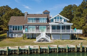 A two-story house with a dock, a covered deck, and a staircase leading to the upper level. - Sunrise View | Waterfront, Kayaks, Gorgeous Sunrises! (Chincoteague Island)