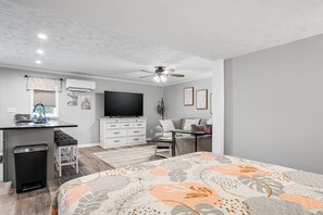 A modern bedroom with a bed, a desk, a TV, and a ceiling fan.