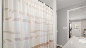 A bathroom with a shower curtain, a sink, and a mirror. - Grandpa's Cottage | Cute, clean and cozy studio apartment! (Chincoteague Island)